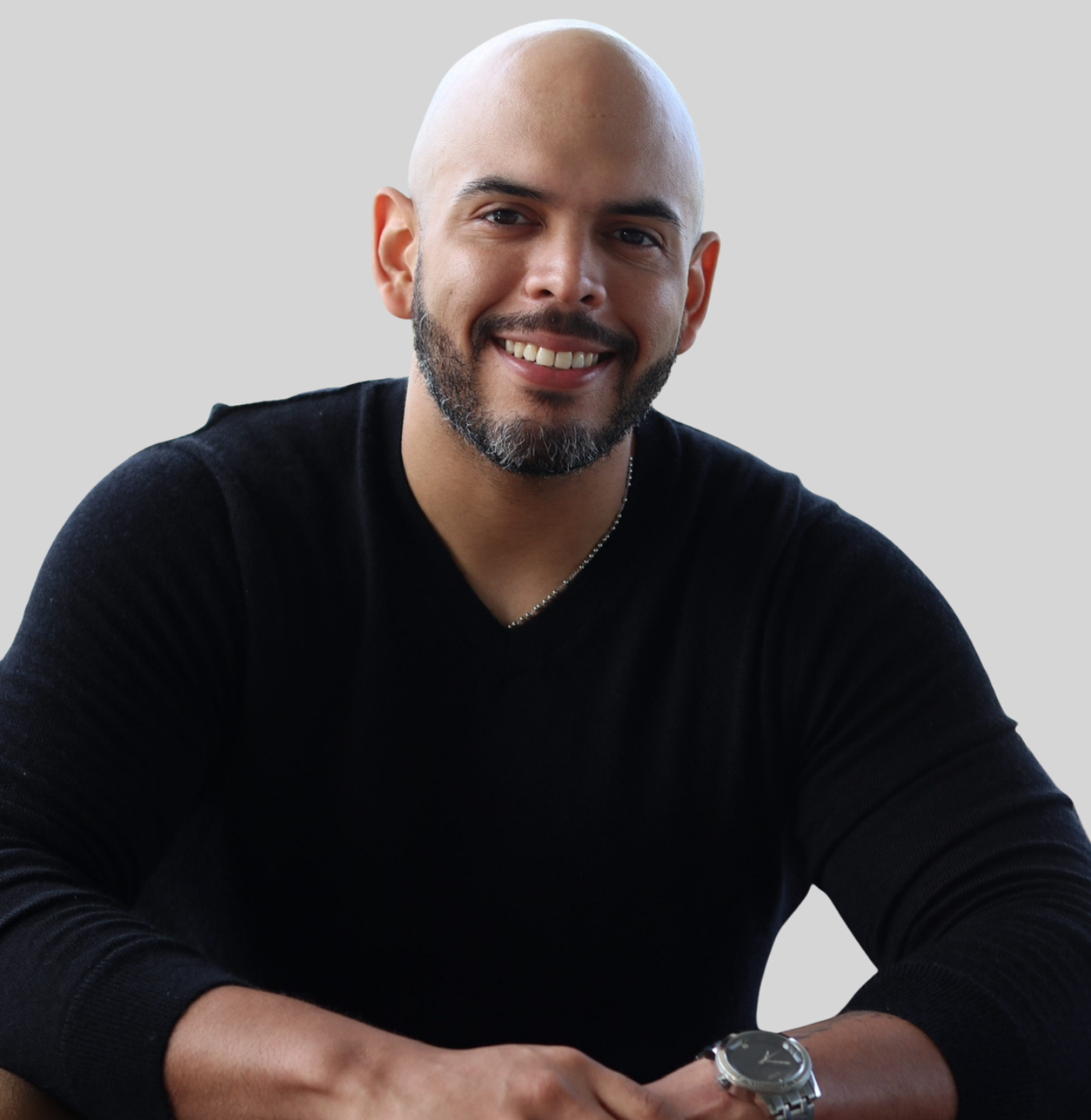 Smiling man with a shaved head and beard, wearing a black sweater, against a light gray background.