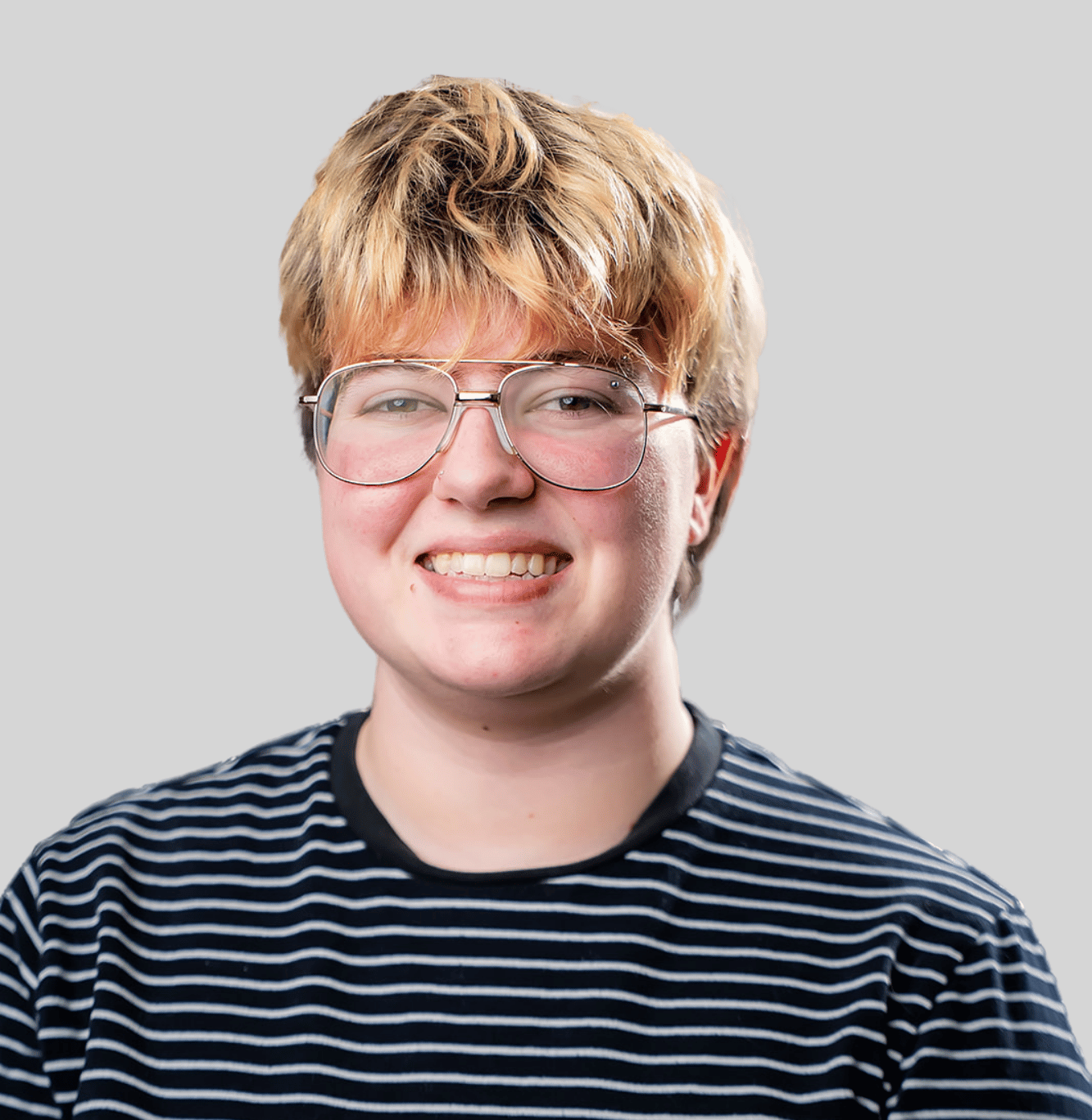 Person with short blond hair and metal glasses smiles at the camera, wearing a navy striped shirt against a light gray background.